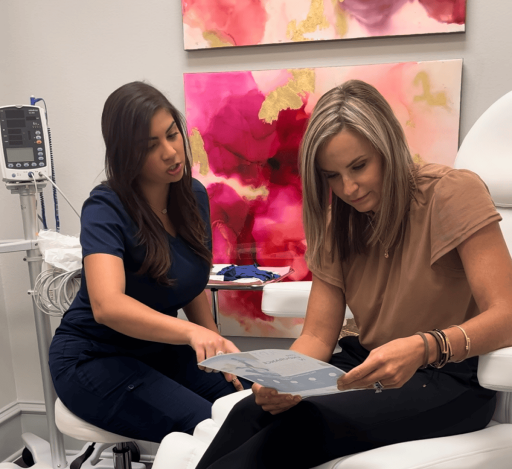 A SCULPT provider a female patient look over a one-sheet while sitting in a comfortable treatment room. They're discussing her weight loss journey, including how GLP-1 in Frisco can help.