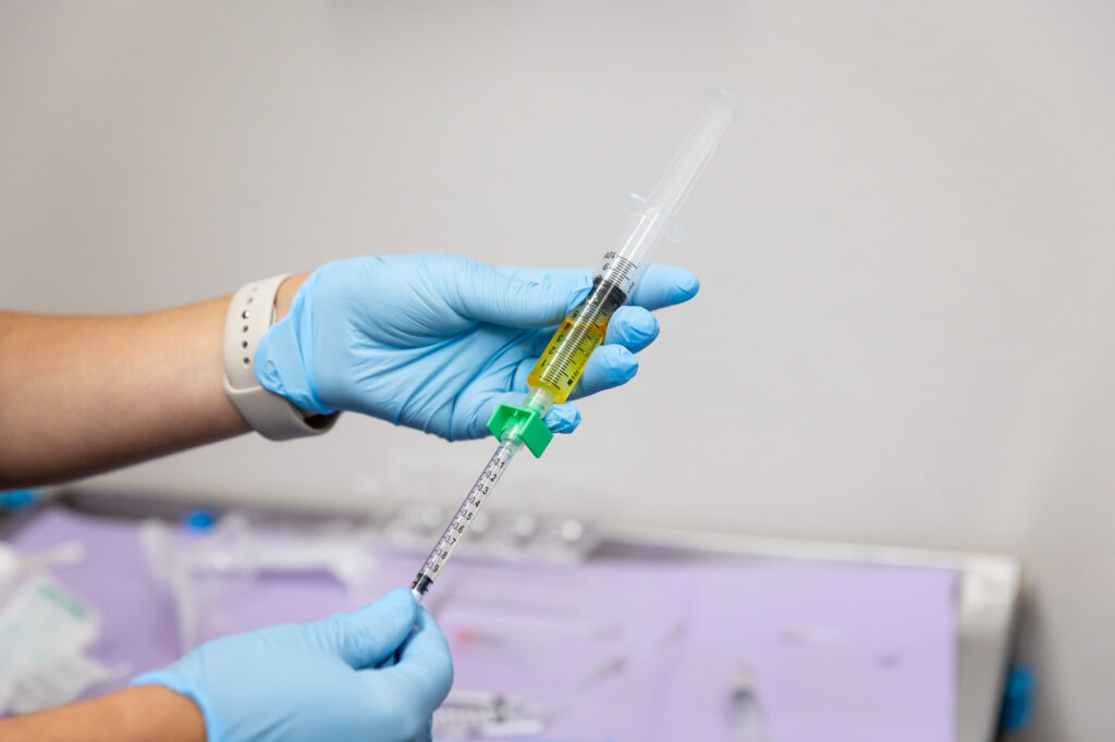 A SCULPT providers hands, wearing blue medical gloves, holds a hypodermic ready for injection. This is part of therapy involving PRP injections in Dallas.