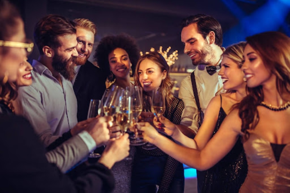 A group of happy, attractive adults raise champagne glasses in a toast while at a nightclub. Some of them have refound their vitality to enjoy fun together after having IV therapy in Dallas at SCULPT.